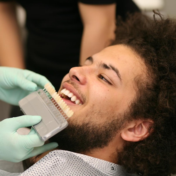 A man smiles as he is presented with a visual aid showing different shades of teeth